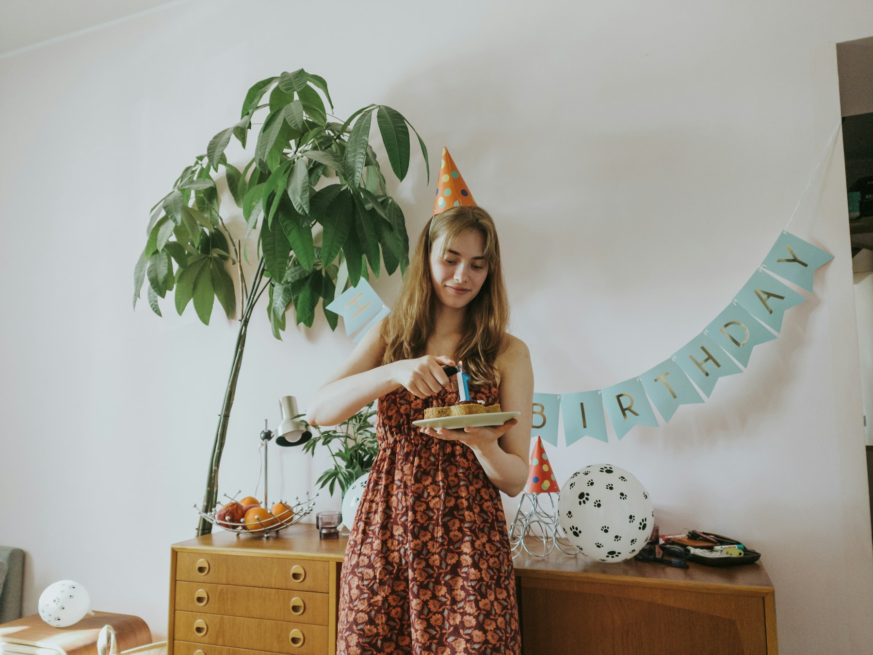 A woman wearing a party hat lighting a candle on her birthday cake