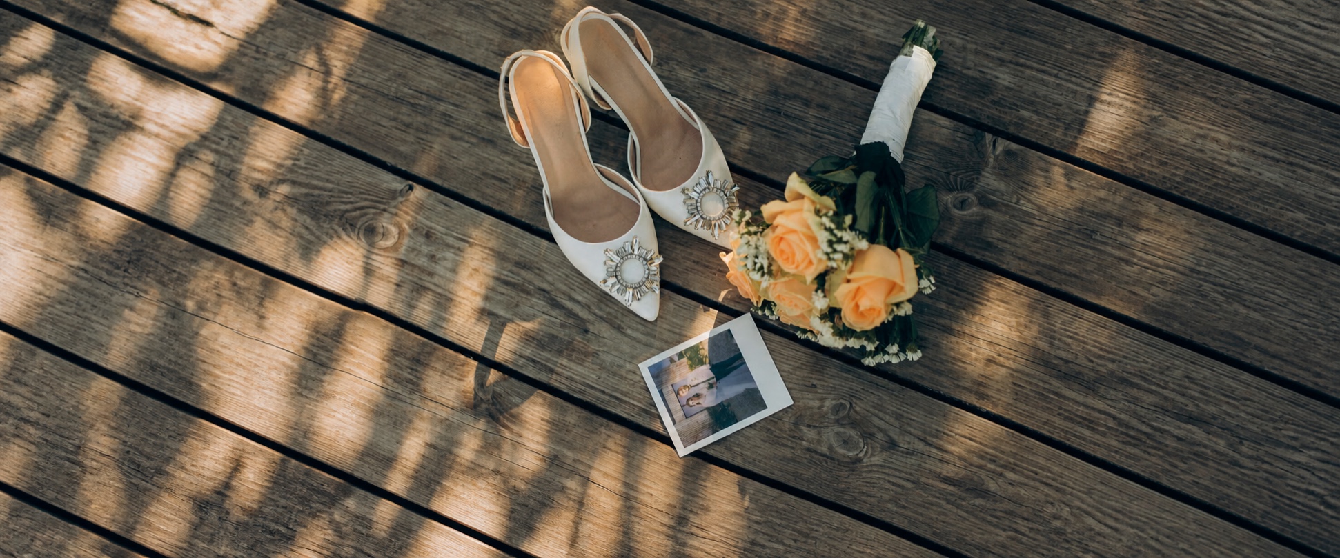 Ivory bridal shoes, a peach rose bouquet and an instant photo arranged on wooden boards