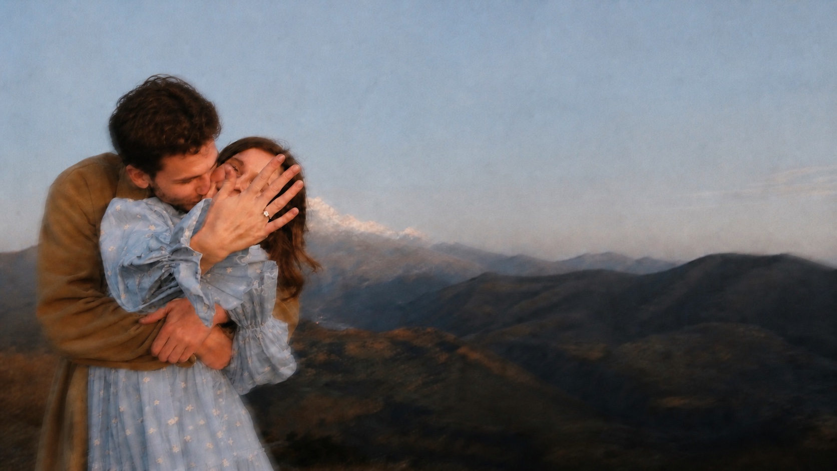 A softly motion-blurred candid photo of Alex embracing and kissing Sam in a powder-blue dress as she shows her engagement ring against a mountain landscape